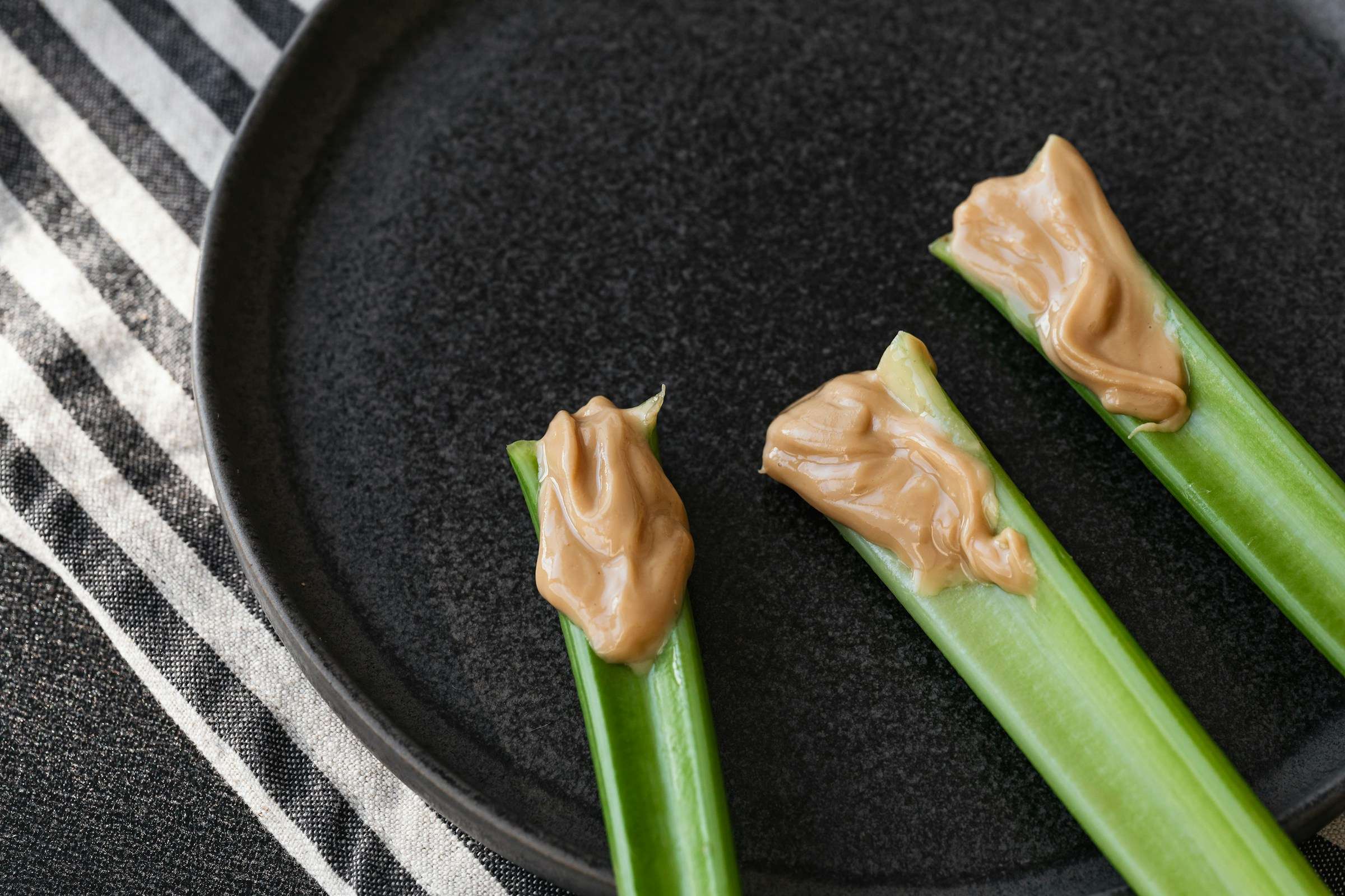 A black plate topped with celery and peanut butter