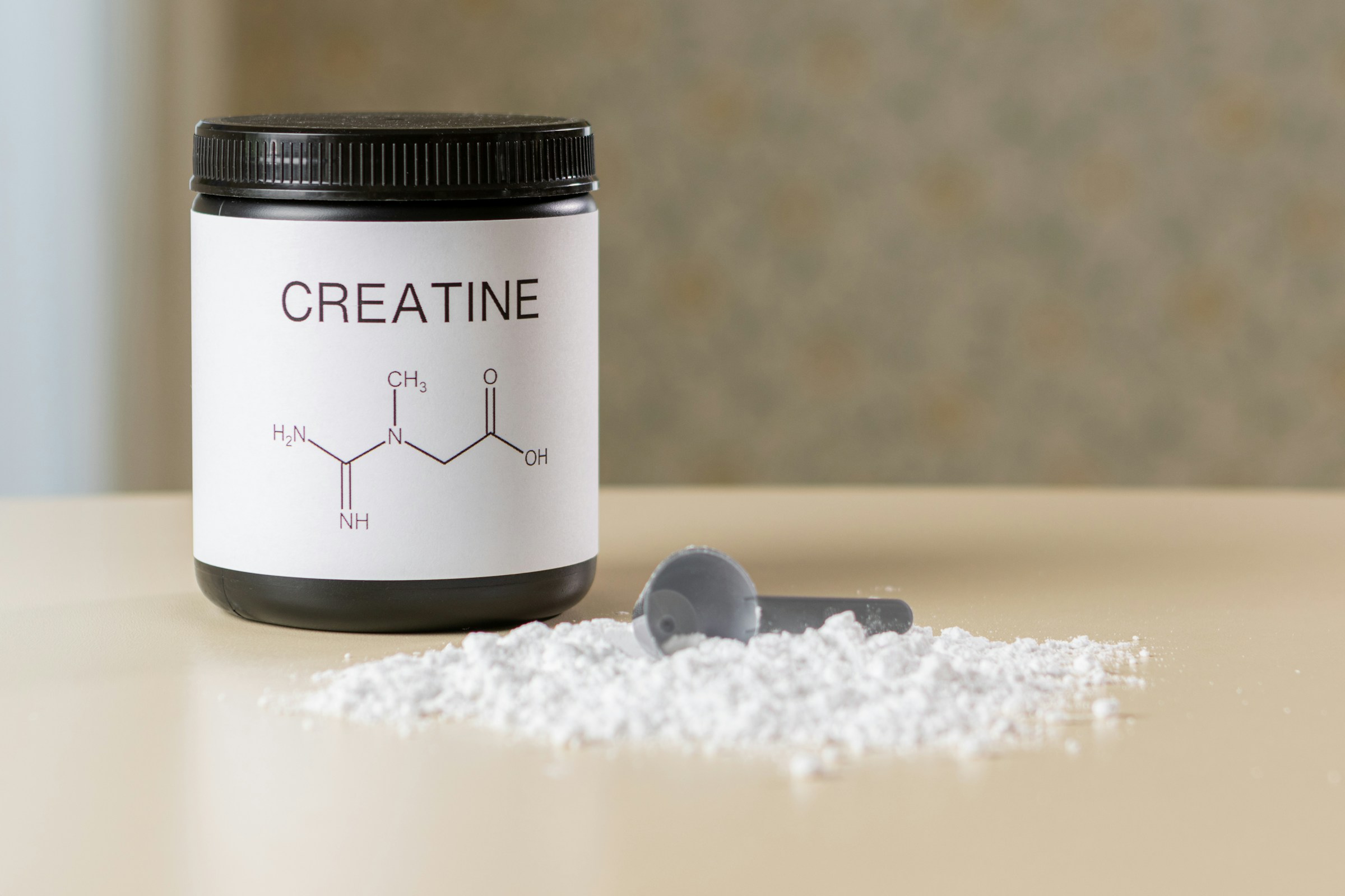 A bottle of Creatine next to a scoop of it