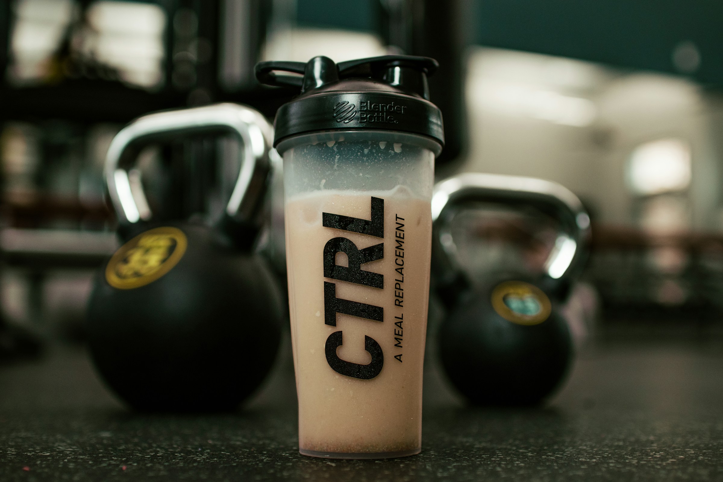 Protein shake on the floor, front layer with weights on the background out of focus