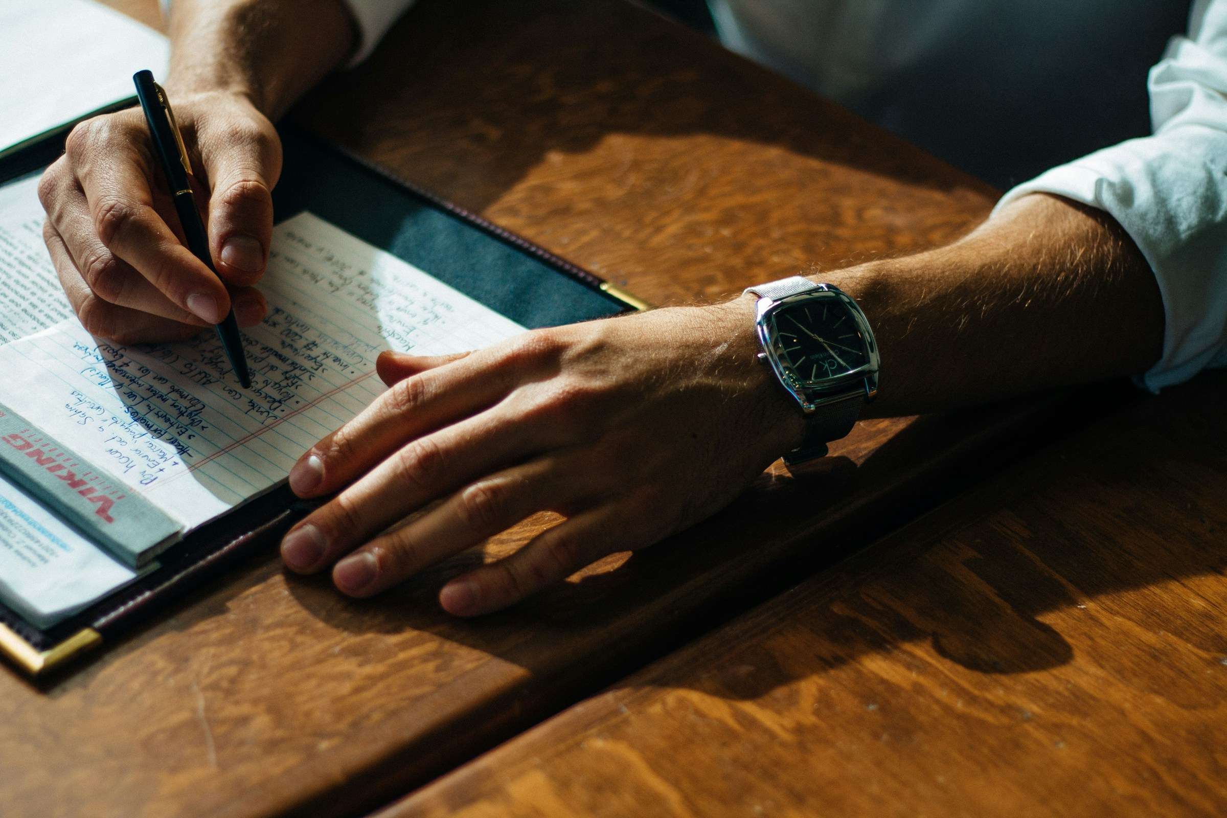 Person writing on paper leaning on brown table